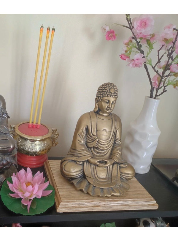 A decorative Buddha statue in a seated meditation pose, finished in a warm bronze tone and mounted on an oak base. Its calm expression and detailed design make it a peaceful and elegant display piece.