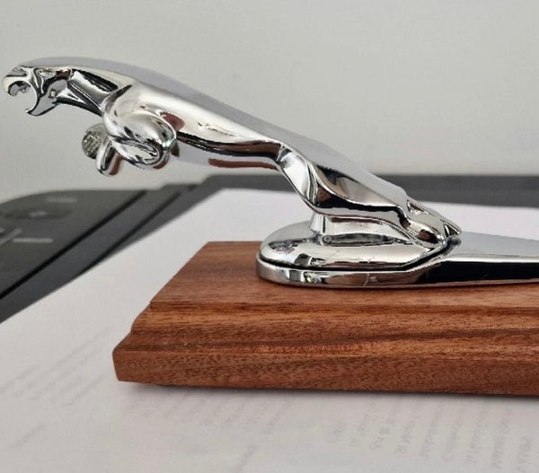 A chrome leaping jaguar hood ornament mounted on a mahogany display base. The sleek design captures the classic style of vintage Jaguar car mascots, making it a striking decorative piece.