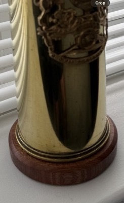 A polished brass artillery shell casing repurposed as a decorative vase, mounted on a mahogany base. Creates a striking and unique display piece.