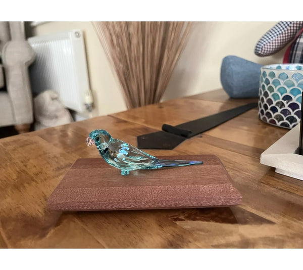 A small decorative glass bird mounted on a mahogany base. The delicate blue glass and simple display create an elegant and eye-catching ornament.