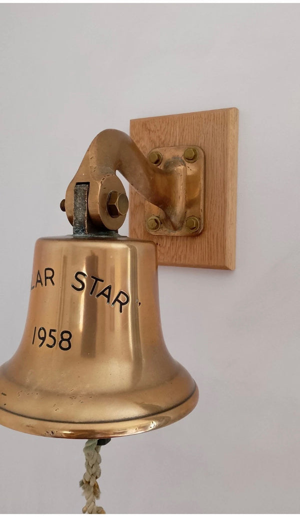 A polished brass ship’s bell engraved “Polar Star 1958,” mounted on a wooden backing plate. Its classic maritime design and rope pull make it a striking nautical decorative piece. ⚓