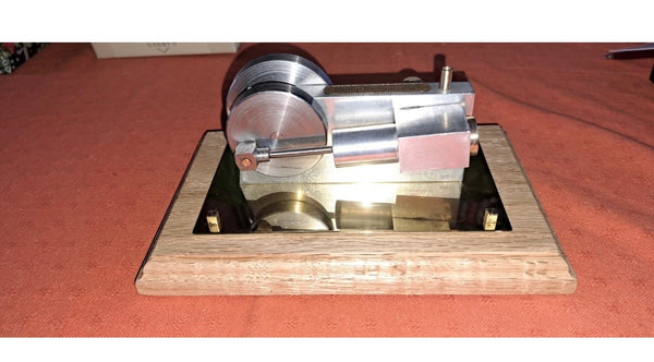 A finely crafted miniature steam engine mounted on a wooden display base with a mirrored plate. Its polished metal components and detailed engineering make it an eye-catching mechanical display piece.