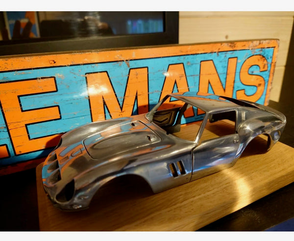 A detailed metal model car body shell displayed on an oak base. Its polished finish and classic sports car shape make it a striking piece for automotive enthusiasts.