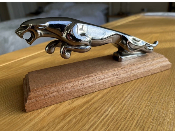 A chrome leaping jaguar ornament mounted on a polished  mahogany base. Its sleek, iconic design makes it a striking display piece for classic car enthusiasts.