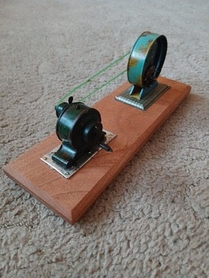 A vintage mechanical model mounted on a polished mahogany base, featuring a small motor and flywheel connected by a belt. Its classic engineering design makes it an interesting and decorative display piece.