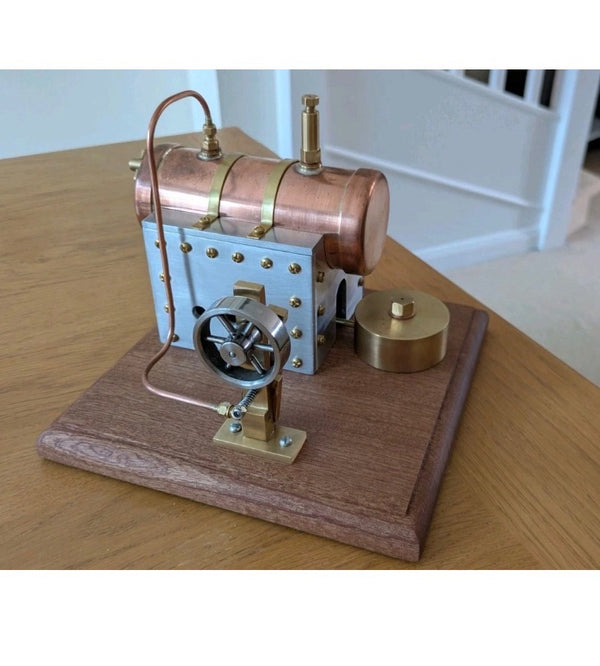 A detailed miniature steam engine model featuring copper, brass, and metal components mounted on a mahogany base. The finely crafted engineering makes it an impressive mechanical display piece.