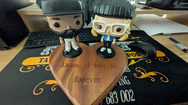 Two collectible figures displayed on a handcrafted heart-shaped mahogany base engraved “Dean + Meesh forever.” A unique and personal decorative piece celebrating a special relationship.