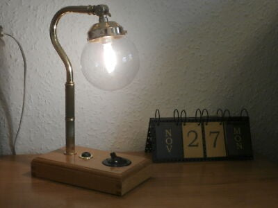 A stylish desk lamp with a curved brass arm and a clear globe bulb, mounted on a solid oak base with a switch. Its minimalist, vintage-inspired design adds a warm and elegant touch to any workspace. 