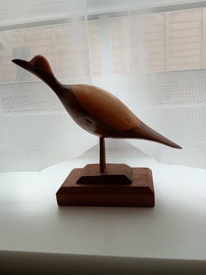 A beautifully crafted wooden bird sculpture mounted on a matching wooden display base. Its smooth, elegant shape and natural finish make it a timeless decorative piece.