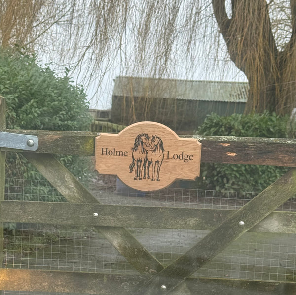 A handcrafted wooden sign engraved “Holme Lodge” featuring a detailed illustration of two horses. The natural wood finish and clean engraving make it a beautiful and welcoming entrance sign.